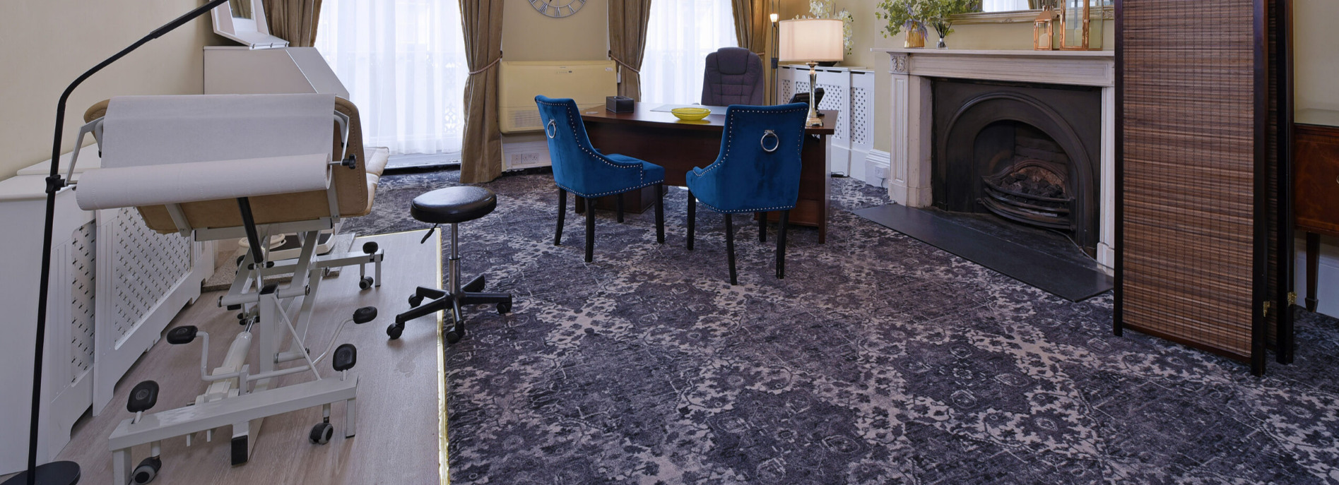 Consulting room with examination couch, desk and blue velvet chairs at 10 Harley Street